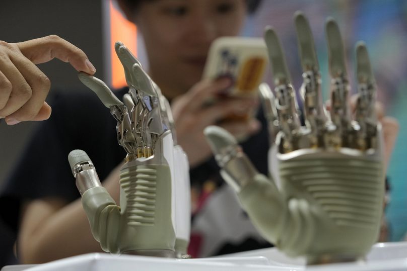 Un visiteur touche la main d'un robot humanoïde exposé sur un stand d'exposition d'IA à Shanghai, le 4 juillet 2024