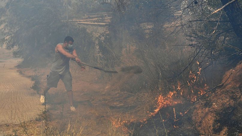 Un volontaire jette de la terre avec une pelle sur les flammes, à Dioni, au nord-est d'Athènes, en Grèce, le 12 août.