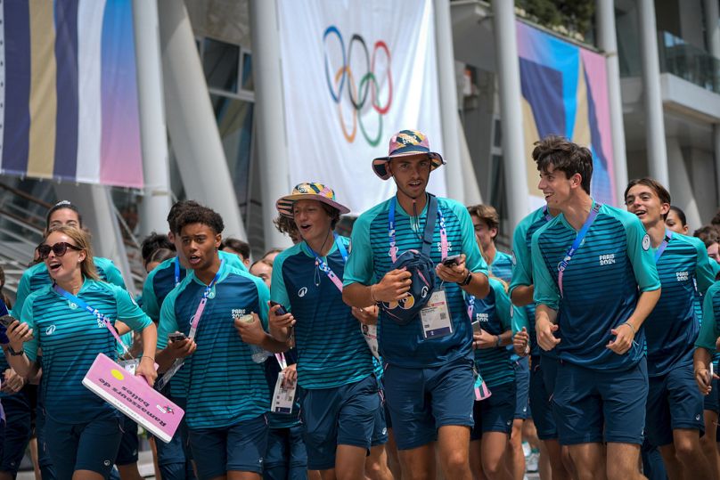 Des bénévoles courent devant le court central Philippe Chatrier à leur arrivée au stade Roland Garros avant la compétition de tennis, aux Jeux olympiques d'été de 2024