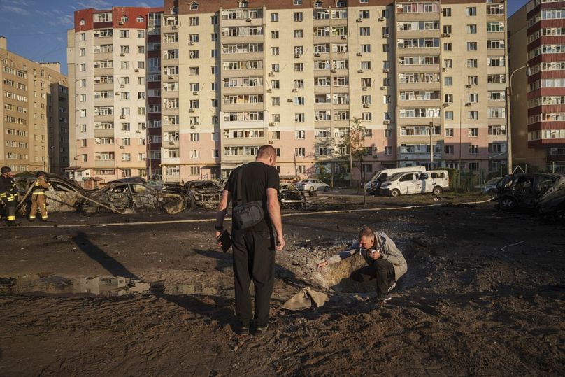 Des jeunes hommes regardent des éclats d'obus après une frappe aérienne russe sur un quartier résidentiel de Soumy, en Ukraine, le samedi 17 août 2024.