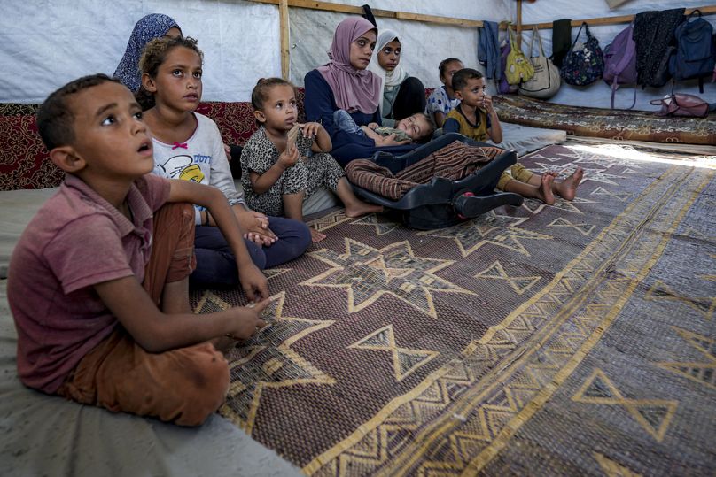 Le nourrisson déplacé Abdel-Rahman Abu El-Jedian, âgé de 11 mois et atteint de polio, est porté par sa mère, au centre, dans un camp de tentes de fortune à Deir al-Balah, dans le centre de Gaza.