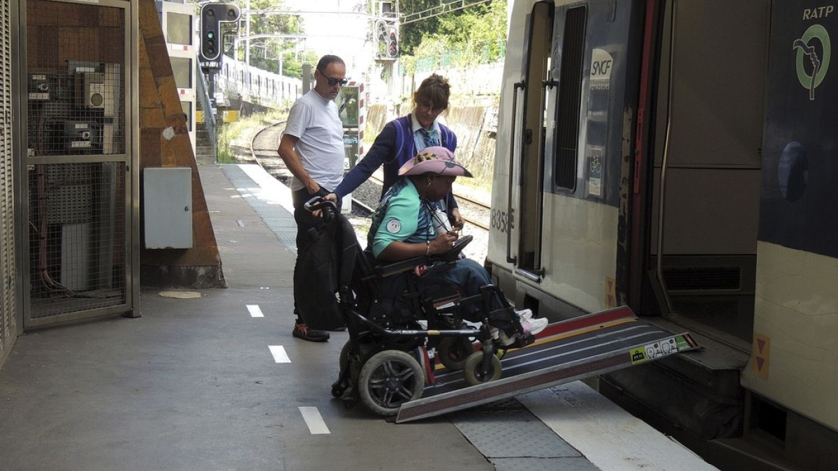 A volunteer for the Paris 2024 Olympic and Paralympic Games navigates a ramp to join a RER train with the help of rail agents