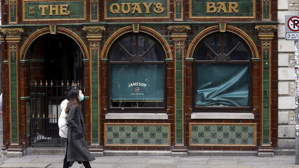 A woman wearing a face mask passes a closed pub in the temple bar area of Dublin city center, Monday, March, 16, 2020.