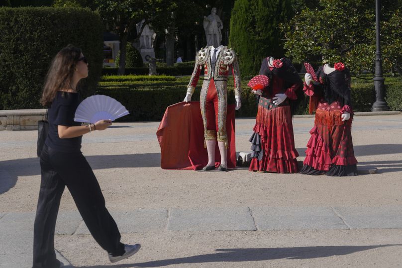 Une femme s'évente en passant devant un matador et des découpes de robes traditionnelles derrière lesquelles les touristes posent pour des photos à Madrid, en Espagne, le vendredi 19 juillet 2024.