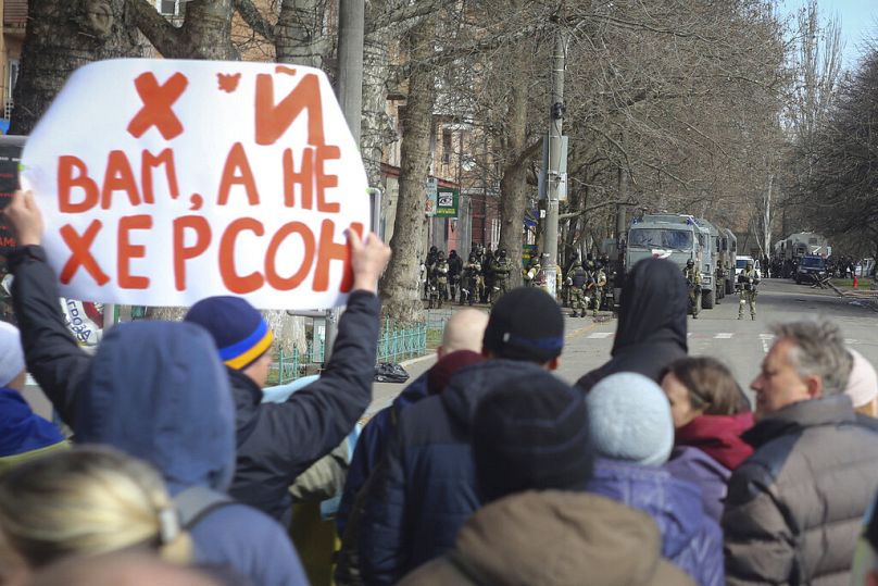 Des gens se tiennent devant les troupes russes dans une rue lors d'un rassemblement contre l'occupation russe à Kherson, le 14 mars 2022