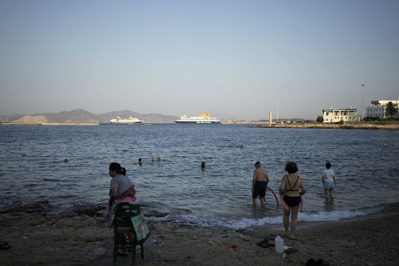 Les gens nagent sur une petite plage, lors d'une chaude matinée dans la ville portuaire du Pirée à Athènes.