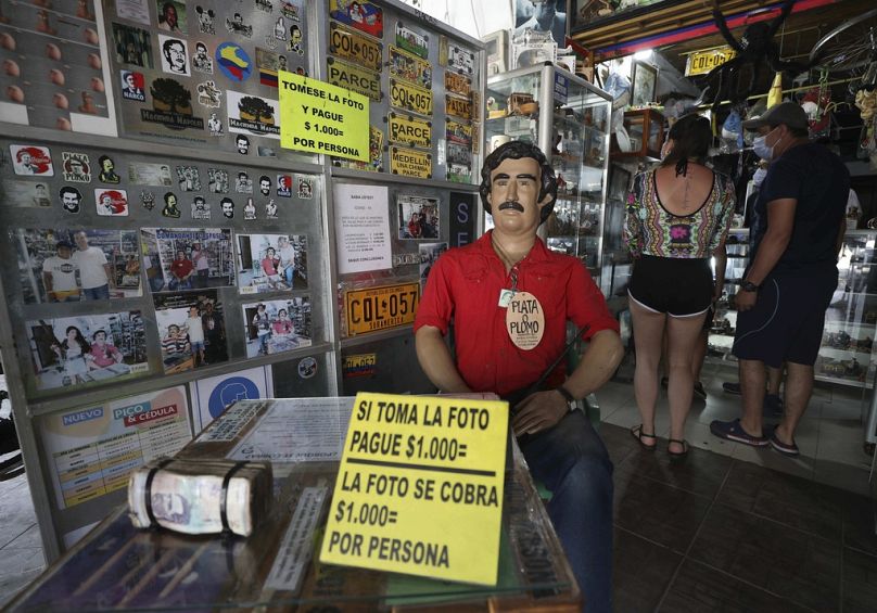 Des touristes achètent des souvenirs du défunt baron de la drogue Pablo Escobar, représentés par une statue avec un panneau indiquant que toute personne prenant des photos à l'intérieur d'un magasin à Doradal sera facturée.