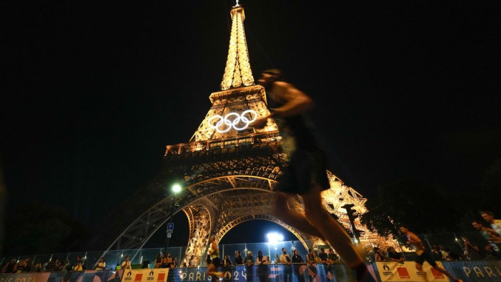 Spectators stand at the base of the Eiffel Tower as they watch runners participate in the Pour Tous marathon, at the 2024 Summer Olympics, in Paris, Saturday, Aug. 10, 2024.