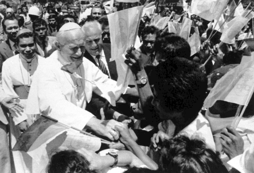 Cette photo d'archives du 12 octobre 1989 montre le pape Jean-Paul II serrant la main d'étudiants locaux brandissant des drapeaux à son arrivée à Dili, au Timor oriental. Le pape François a parcouru 32 814 km