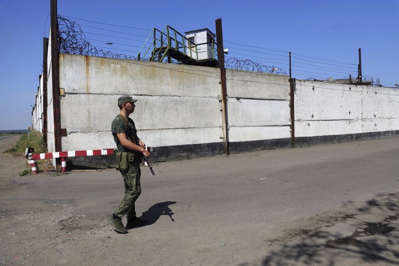 A soldier stand guard next to a wall of a prison in Olenivka, in an area controlled by Russian-backed separatist forces, eastern Ukraine, Friday, July 29, 2022.