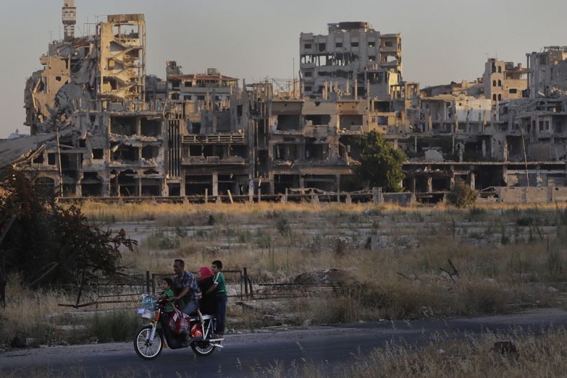 Des gens roulent à moto devant des bâtiments endommagés dans la vieille ville de Homs, août 2018