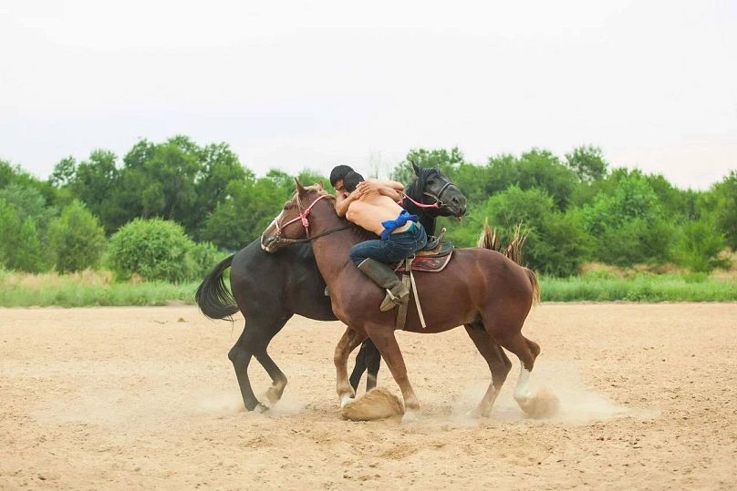 Audaryspaq voit deux concurrents, chacun à cheval, lutter pour tirer l'autre de son cheval.