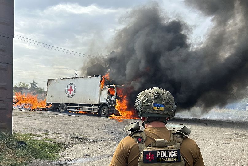 Un policier regarde un véhicule de la Croix-Rouge en feu qui a été détruit lors d'une frappe russe dans la région de Donetsk, le 12 septembre 2024