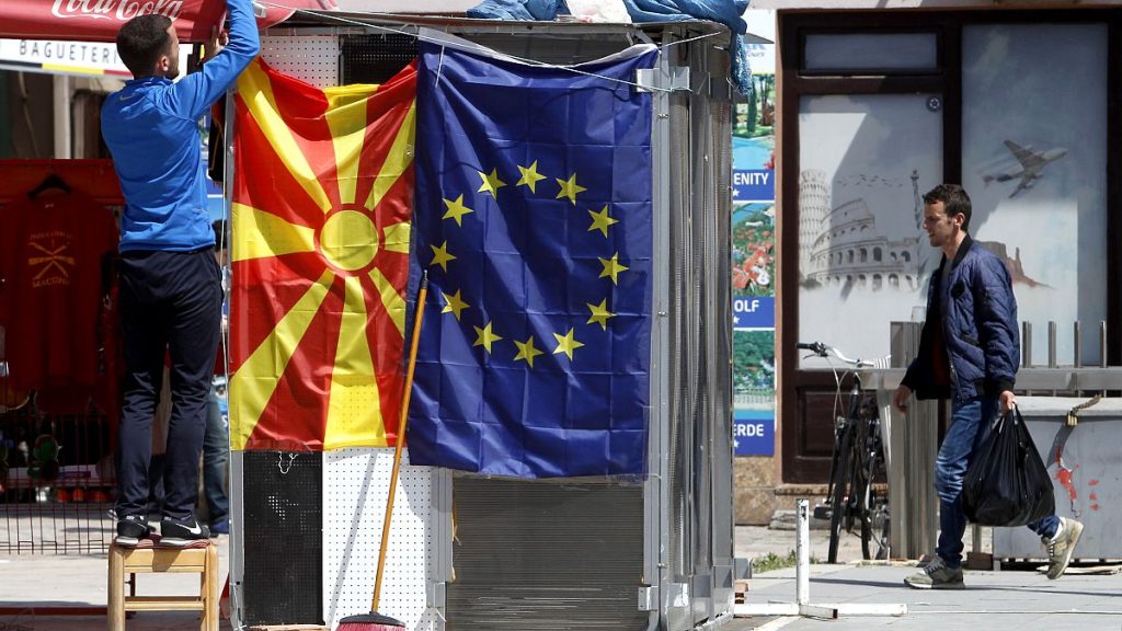 A street vendor fixes a North Macedonia flag next to an EU flag in a street in Skopje, May 3, 2019