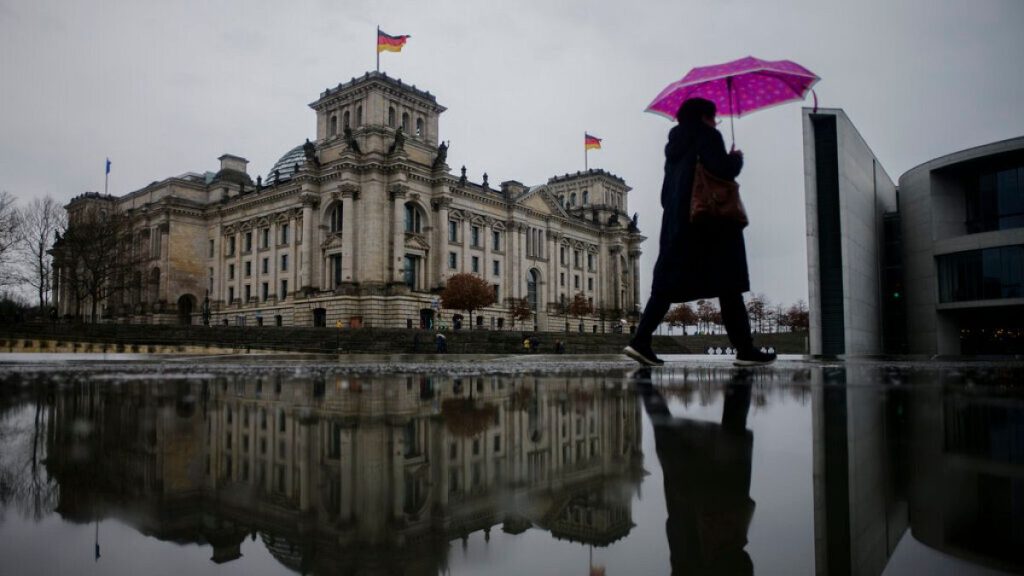 A person with an umbrella walks through the government district in front of the Reichstag building, the house of German parliament Bundestag,in Berlin, Germany, 2022.