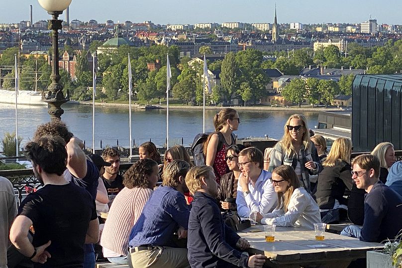 Les gens dégustent des boissons et des collations au soleil du soir sur une terrasse surplombant Stockholm en 2023. Il est interdit de fumer dans les espaces extérieurs des bars et restaurants en Suède.