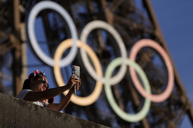 Une personne prend un selfie avec les anneaux olympiques sur la tour Eiffel pendant les Jeux olympiques d'été de 2024, le mardi 6 août 2024, à Paris, France.