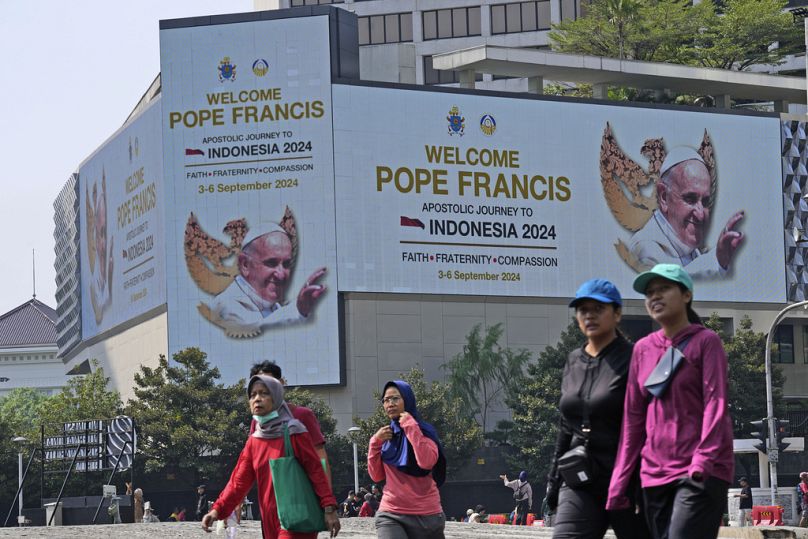 Des gens passent devant un panneau de bienvenue pour le pape François affiché dans la cathédrale de Jakarta, en Indonésie, le dimanche 1er septembre 2024, avant sa visite en Indonésie du 1er septembre au 1er septembre.