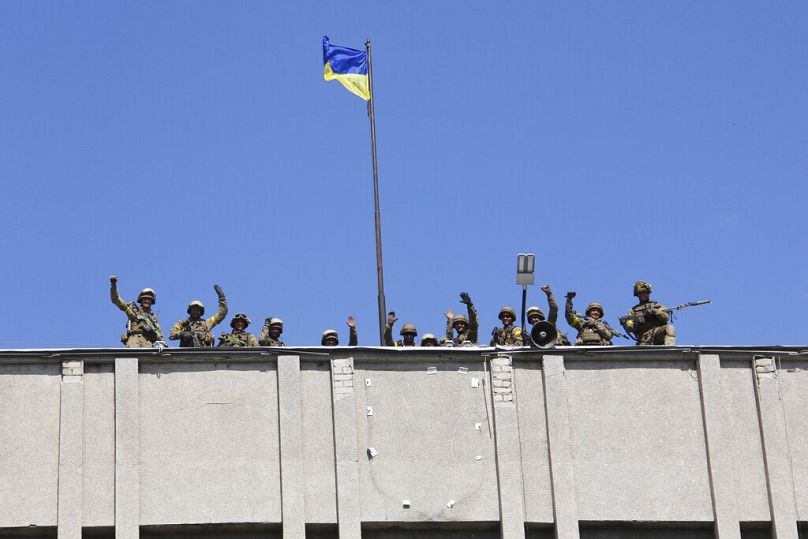 Sur cette photo prise le samedi 5 juillet 2014, des soldats ukrainiens hissent un drapeau ukrainien au-dessus du siège du gouvernement de la ville de Slovyansk, dans l'est de l'Ukraine.