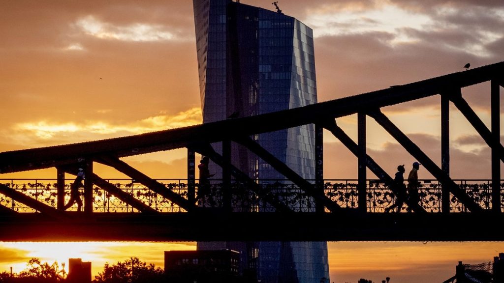 People walk over a bridge near the European Central Bank as the sun rises in Frankfurt, Germany