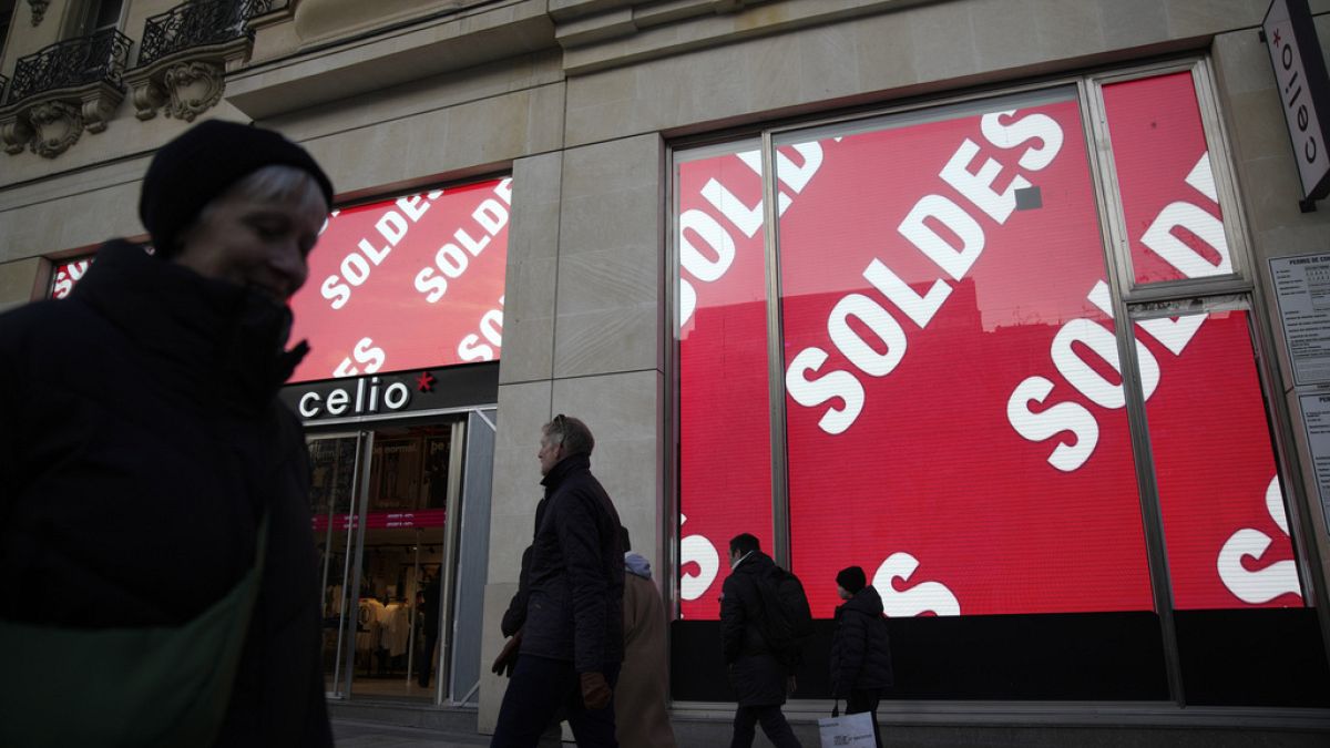 People walk past a shop displaying banners advertising