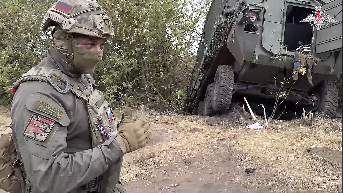 A Russian soldier stands next to a damaged Ukrainian military vehicle in the Russian - Ukrainian border area in the Kursk region, Russia.