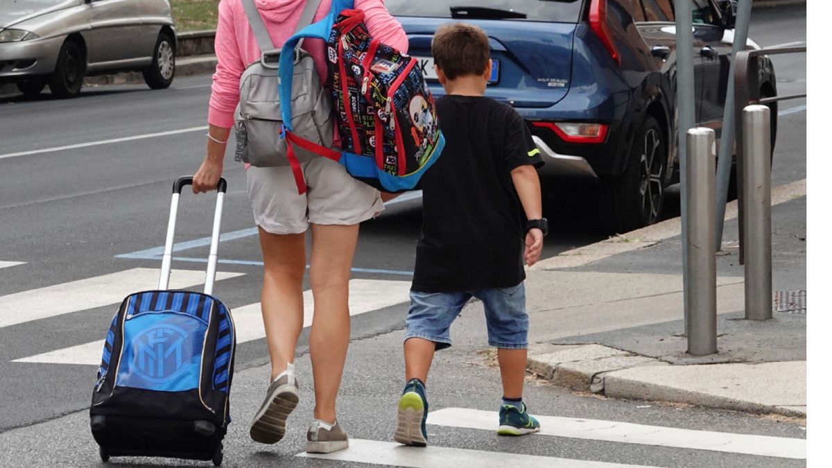 A woman carries backpacks as her son walks after coming out of a primary school, in Milan, Italy