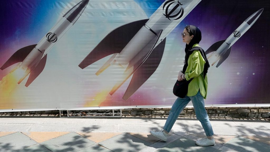 FILE: A woman walks past a banner showing missiles being launched, in northern Tehran, 19 April 2024