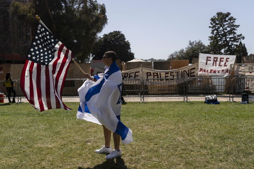 Drapé d'un drapeau israélien, un partisan pro-israélien marche avec un drapeau américain près du campement pro-palestinien sur le campus de l'UCLA à Los Angeles, le 30 avril 2024.