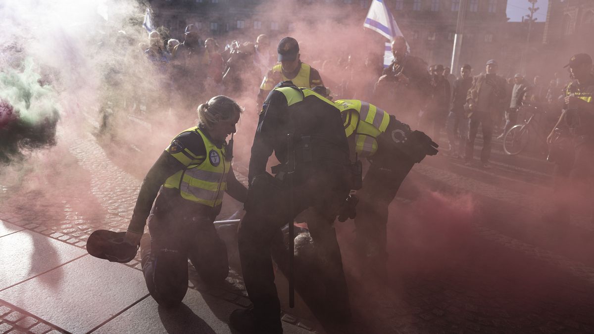 A pro-Palestinian demonstrator with a smoke bomb is detained by police in Amsterdam, Netherlands, Monday, Oct. 7, 2024.