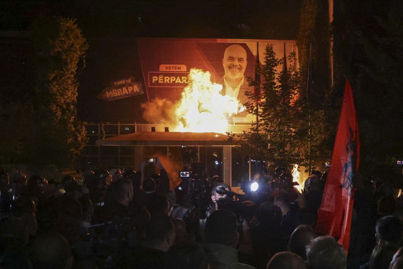 Le feu brûle derrière un cordon de police et devant une affiche représentant le Premier ministre albanais Edi Rama lors d'un rassemblement antigouvernemental à Tirana, en Albanie, le lundi 7 octobre.