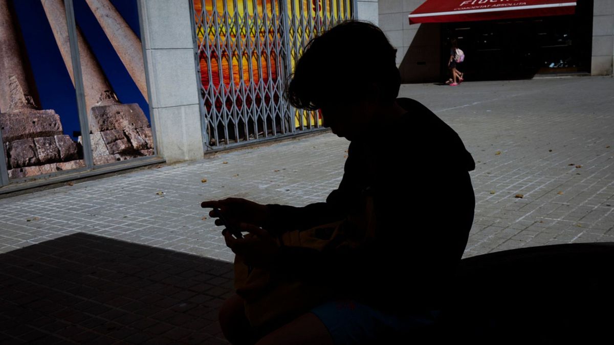 A 12-year-old boy plays with his personal phone outside school in Barcelona, Spain, Monday, June 17, 2024