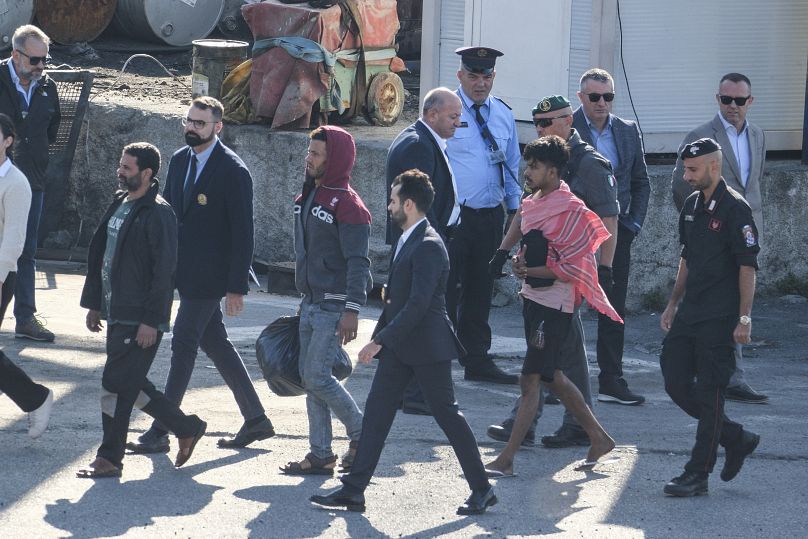 Des migrants et des responsables de la sécurité marchent dans le port de Shengjin après avoir débarqué du navire de la marine italienne Libra, le 16 octobre 2024.