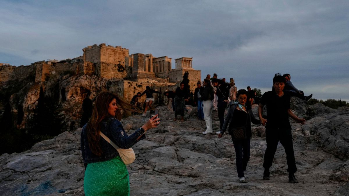 Tourists walk at Areopagus hill in front of the Ancient Acropolis hill as the sun sets in Athens.