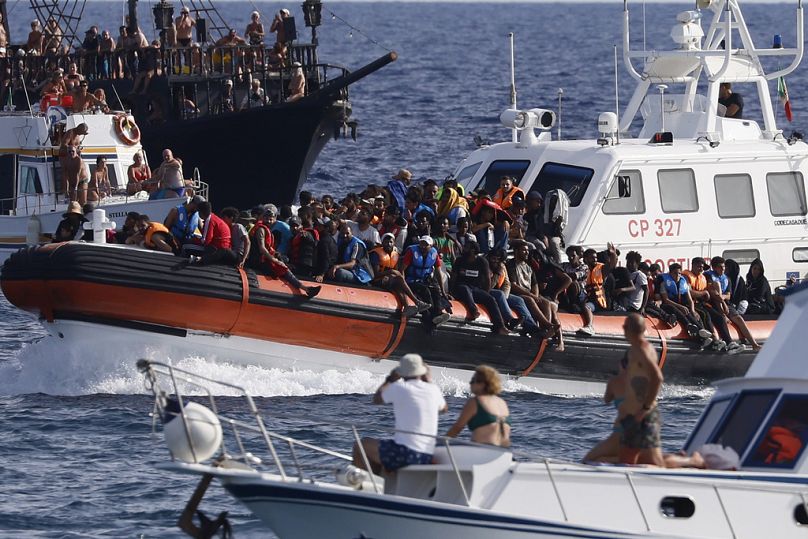 DOSSIER – Un bateau de la Garde côtière italienne transporte des migrants en tant que touristes sur un bateau, au premier plan, en montre, près du port de l'île sicilienne de Lampedusa, en Italie, le 18 septembre 2023.