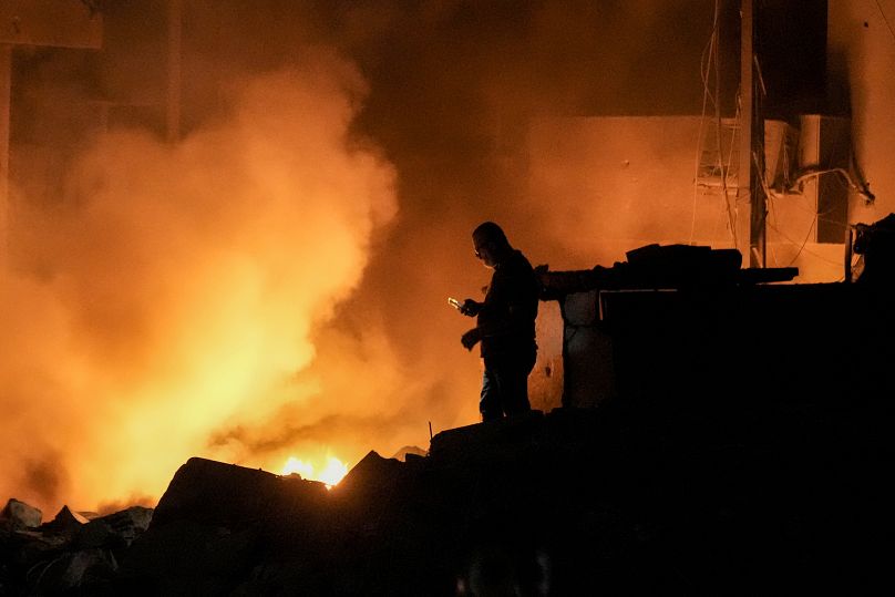 Un homme utilise son téléphone portable alors que les flammes et la fumée montent sur les lieux des bâtiments touchés par une frappe aérienne israélienne dans le centre de Beyrouth, le 10 octobre 2024.