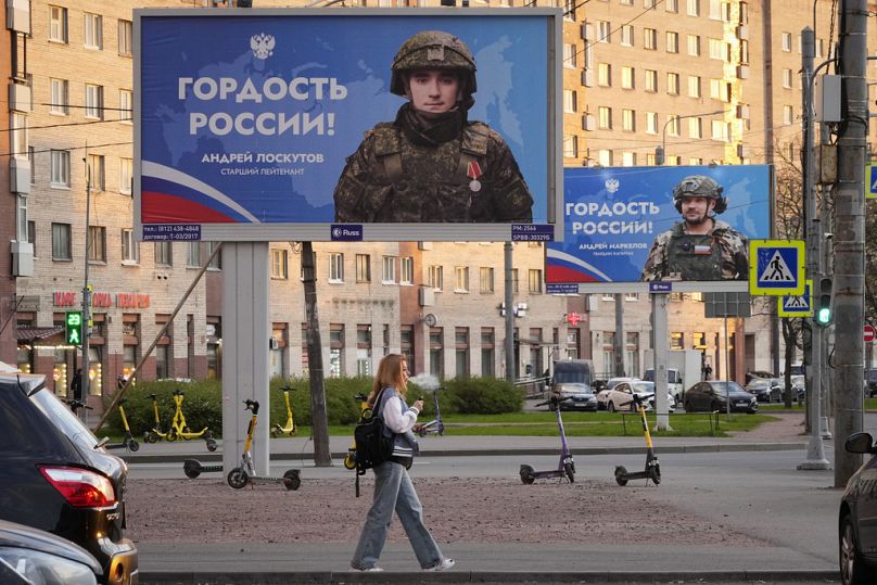 Une femme passe devant des panneaux publicitaires montrant des soldats russes, participants à la guerre en Ukraine, avec les mots en russe « Fierté de la Russie ! », à Saint-Pétersbourg, le 16 mai 2024.