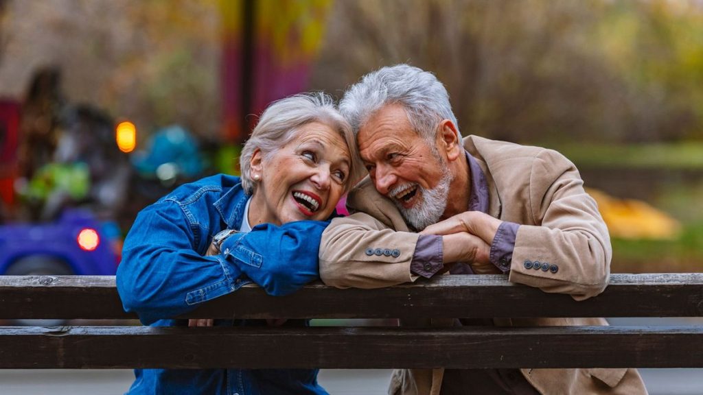 A happy senior couple sitting on a park bench, looking at each other