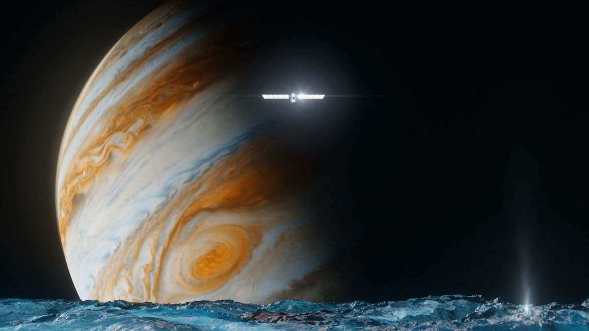 This illustration provided by NASA depicts the Europa Clipper spacecraft above the surface of the moon Europa, foreground, and Jupiter behind.