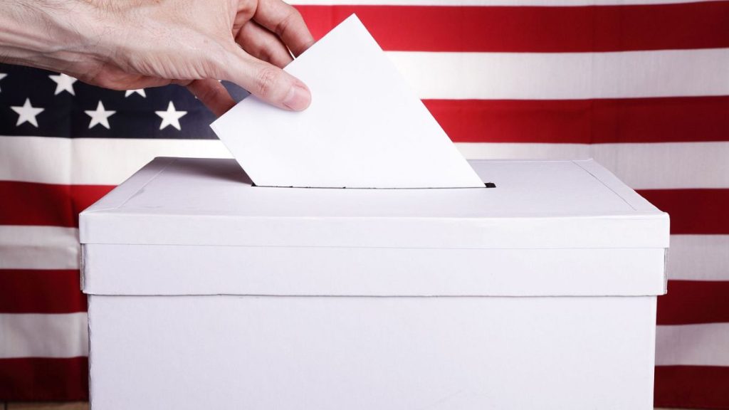 A man casting a vote with a US flag behind him.