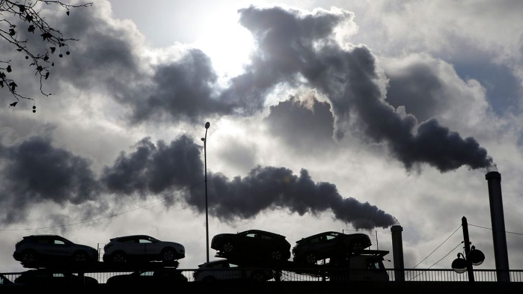 Smoke rises from a factory as a truck loaded with cars crosses a bridge in Paris, France.