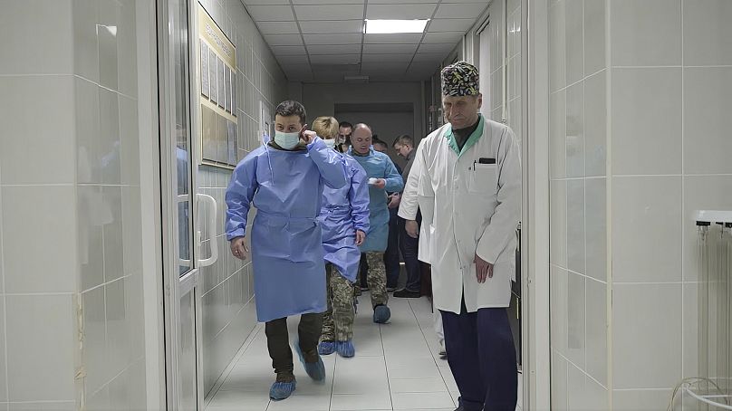 Le président ukrainien Volodymyr Zelenskyy marche dans une blouse chirurgicale et un masque alors qu'il rend visite aux médecins, aux infirmières et aux militaires blessés dans un hôpital de Kiev, en Ukraine.