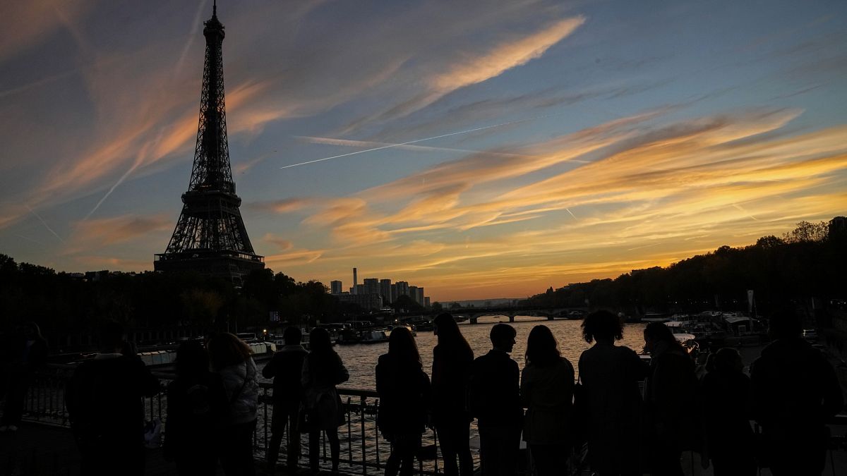 People watch the skyline as the cross the Debilly bridge near Eiffel Tower during sunset in Paris, Saturday, Nov. 12, 2022. (AP Photo/Michel Euler)