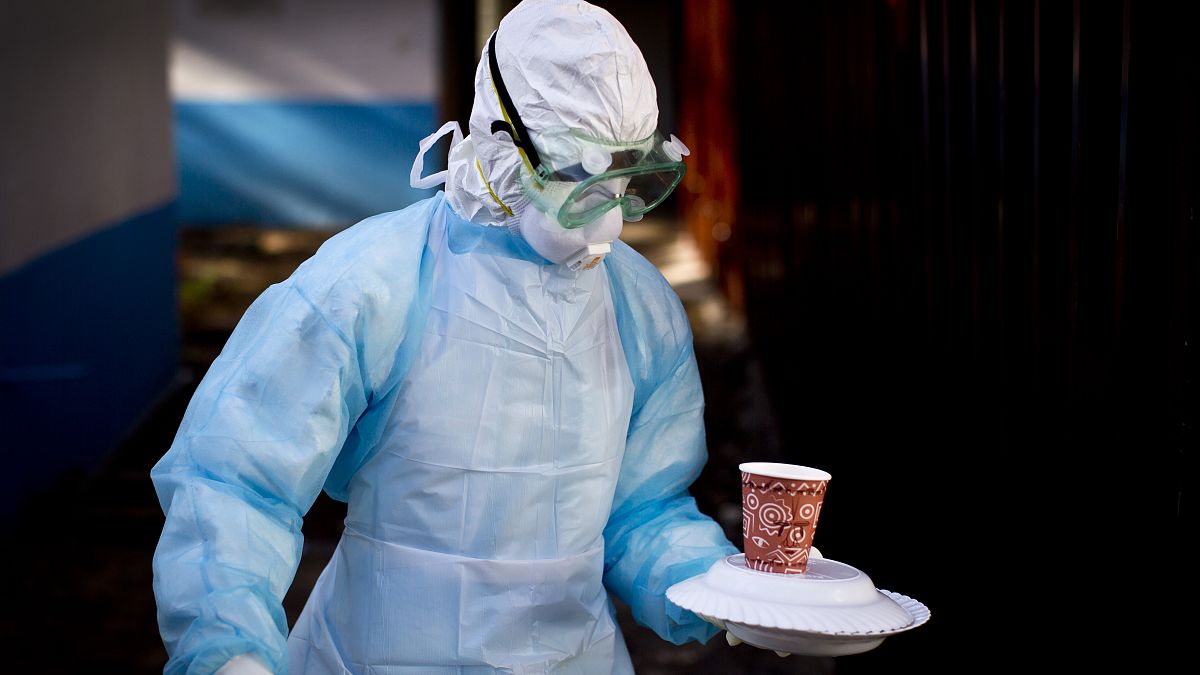 A medical worker wearing full protective equipment carries a meal to an isolation tent housing a man being quarantined for exposure to Marburg, 2014.