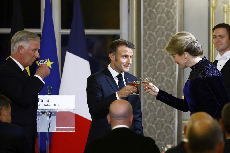 Le président français Emmanuel Macron, au centre, tient un verre pour porter un toast à côté du roi Philippe de Belgique, à gauche, et de la reine Mathilde