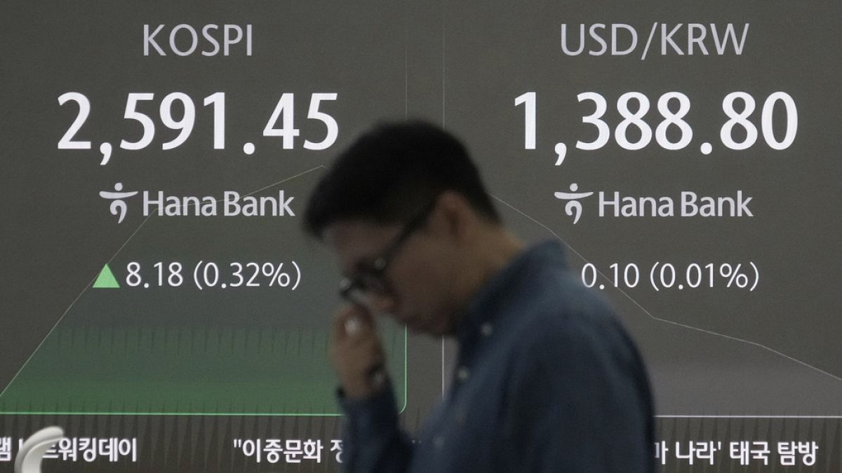 A currency trader works near a screen showing the Korea Composite Stock Price Index (KOSPI).