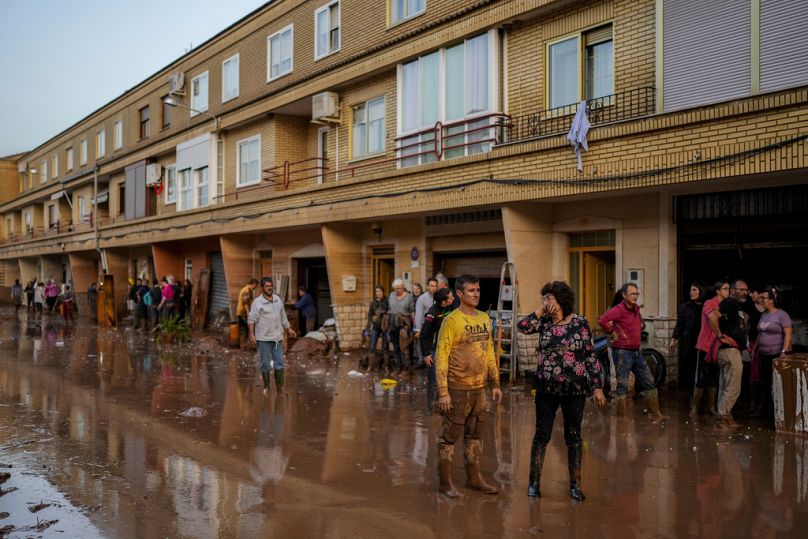 Des gens se tiennent devant leurs maisons touchées par les inondations à Utiel, en Espagne.