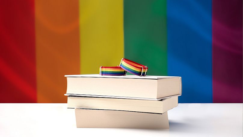 Pile de livres devant un drapeau arc-en-ciel