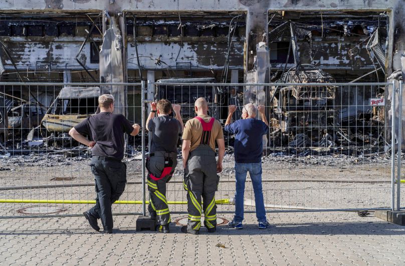 Les pompiers se tiennent près de la clôture et examinent l'équipement brûlé, après l'incendie du nouveau dépôt d'équipement des pompiers volontaires de Stadtallendorf.