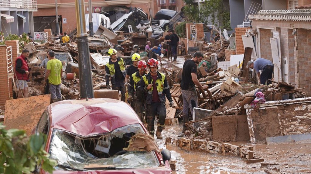 Firefighters walk as people try to clear up the damage after floods in Massanassa, just outside of Valencia, Spain, Friday, Nov. 1, 2024.